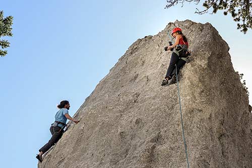 Two people climbing a rock secured with ropes