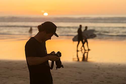 Photographer looking at Canon camera display on the beach at sunset
